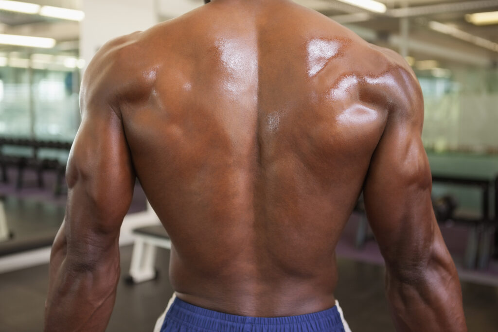 Achteraanzicht van een shirtloze bodybuilder die in de sportschool staat