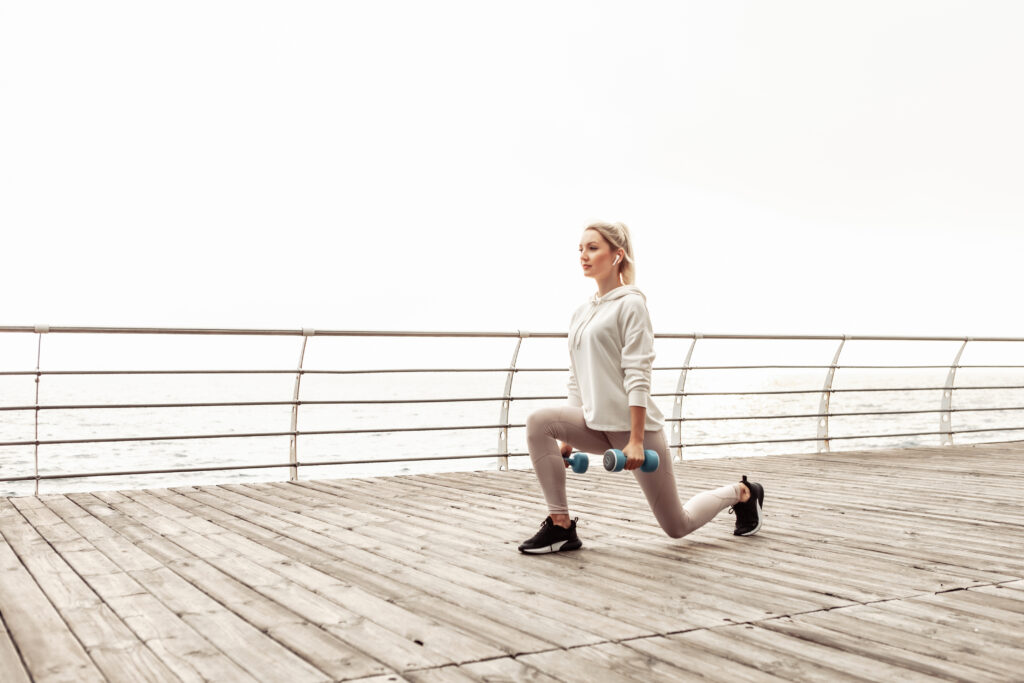 Jonge, gezonde en fitte vrouw oefent lunges met halters op het stadsstrand. Gezonde levensstijl.