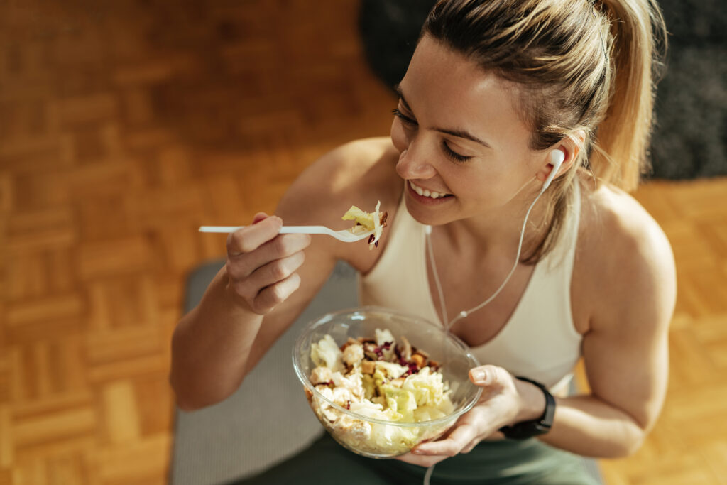 Bovenstaande afbeelding toont een blije sportvrouw die na de training een salade eet.