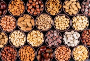Set van pecannoten, pistachenoten, amandelen, pinda's, cashewnoten, pijnboompitten en diverse noten en gedroogd fruit in verschillende mini-schaaltjes op een zwarte stenen achtergrond. Platliggend.