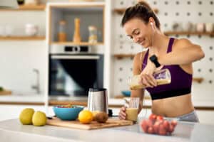 Blije sportvrouw die fruitsmoothie in een glas in de keuken schenkt